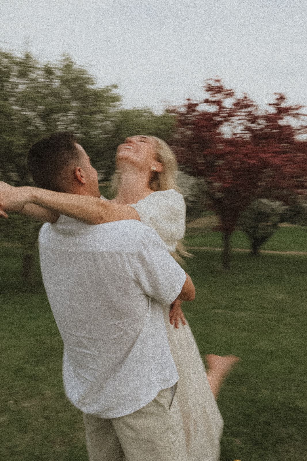 Joyful couple spinning and embracing in a park with red-leaved trees in the background at Minnesota Landscape Arboretum