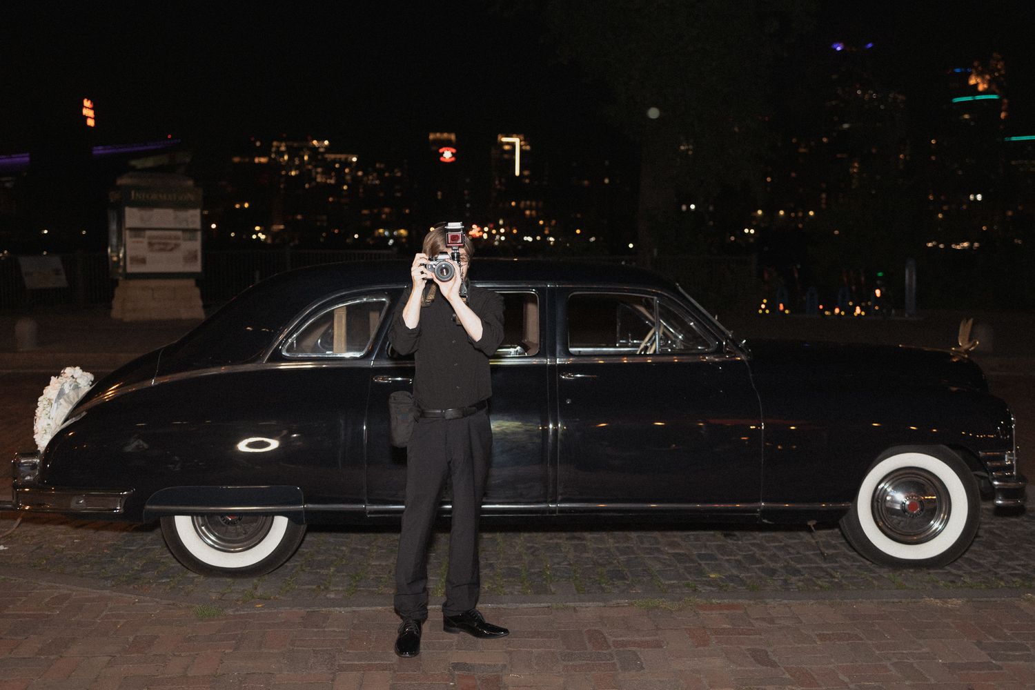 Vintage black Rolls- Royce photographed at night with city lights in background.