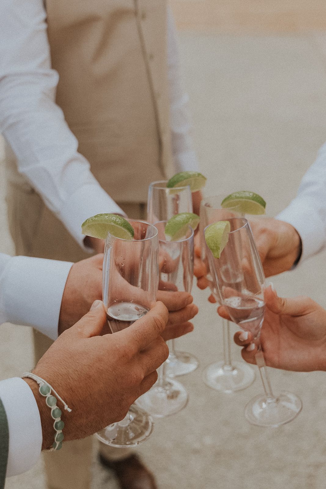 Hands holding cocktail glasses with lime garnishes for a toast at Secrets Akumal Mexico resort wedding