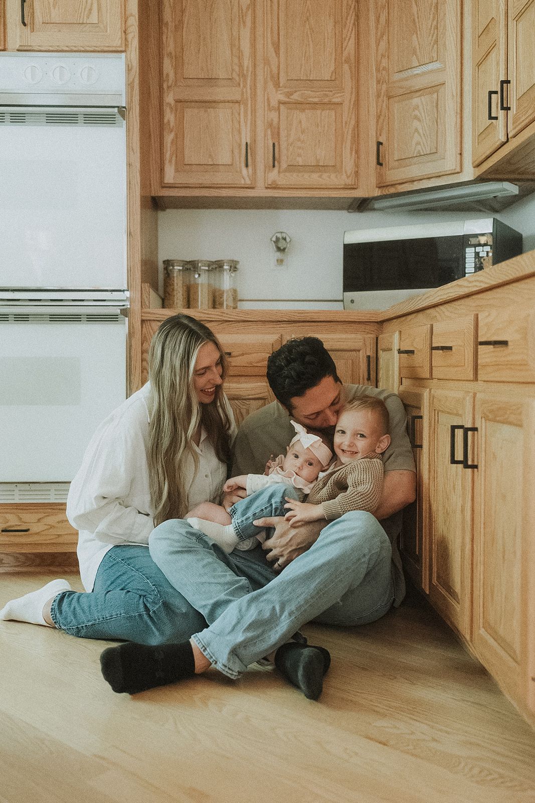 Family Lifestyle picture lying together playfully on hardwood floor in their kitchen.