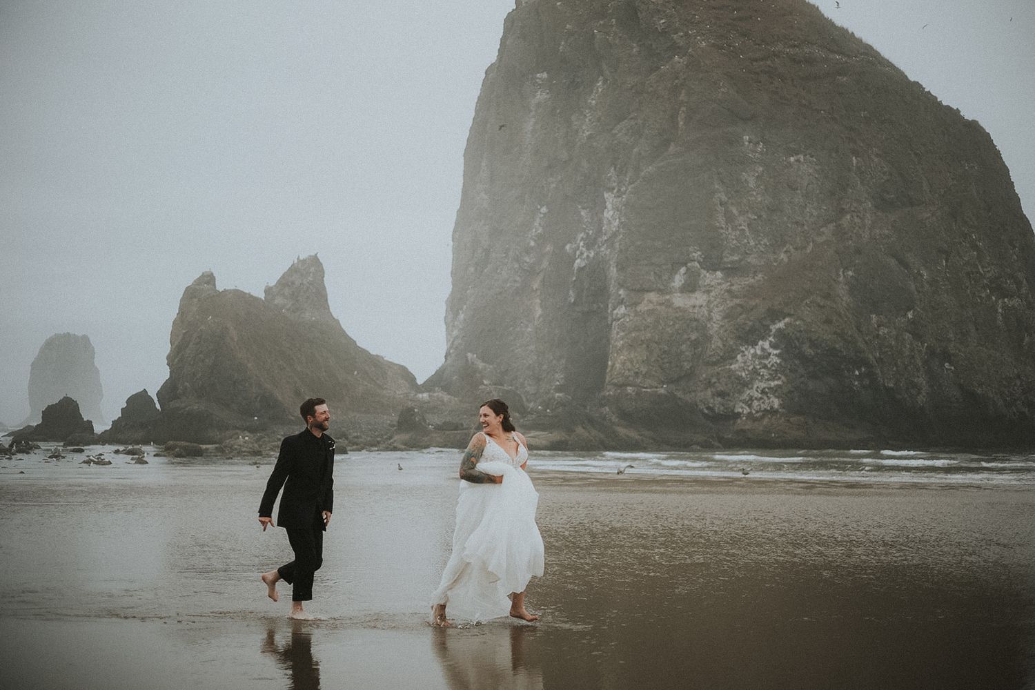 Misty coastal landscape with dramatic rock formations along a foggy beach. Haystack Rock Oregon bride & Groom Running