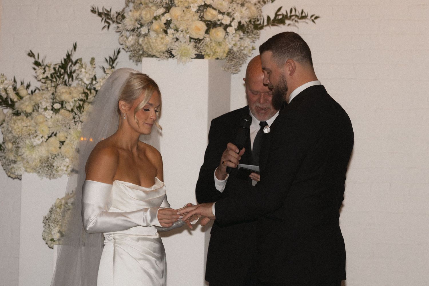 A couple getting married in formal wedding attire, saying vows, exchanging rings under floral decorations at Le Venere in Saint Paul MN