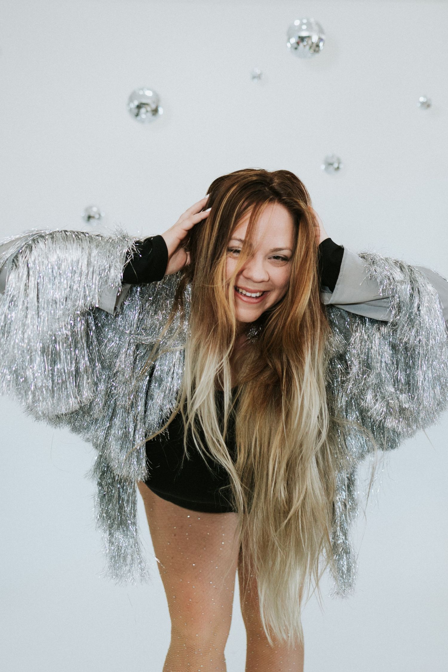 Joyful portrait with sparkly silver jacket and disco balls in minimalist white studio setting.