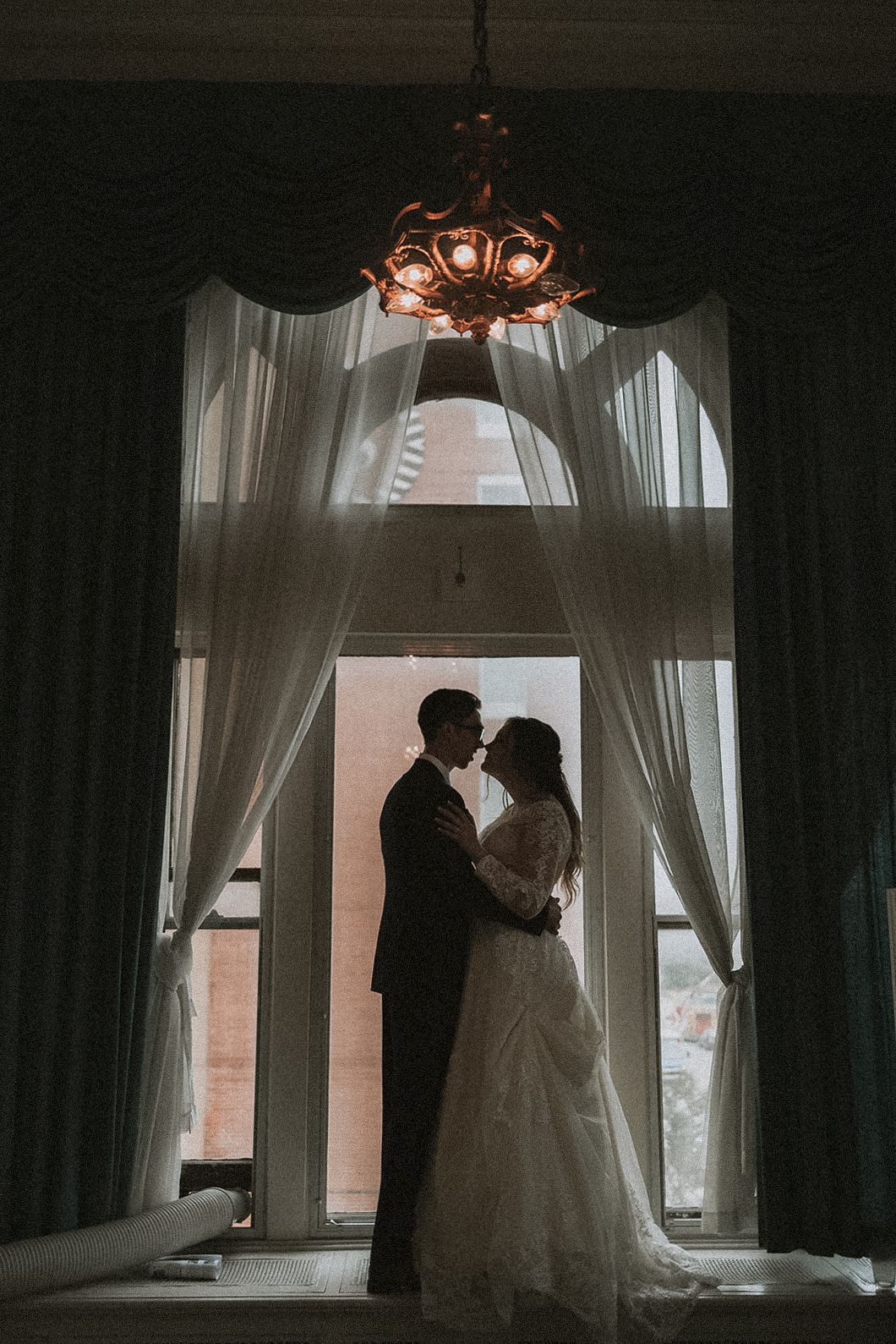 Silhouettes of a couple in wedding attire embrace by a window with sheer curtains at The Greysolon in Duluth Minnesota