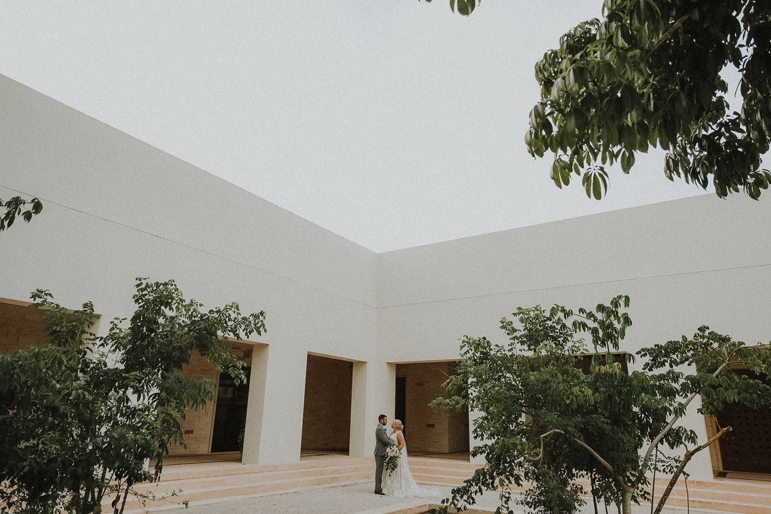 White columns and archways create an elegant architectural setting with tropical greenery at Secrets Akumal Mexico resort wedding