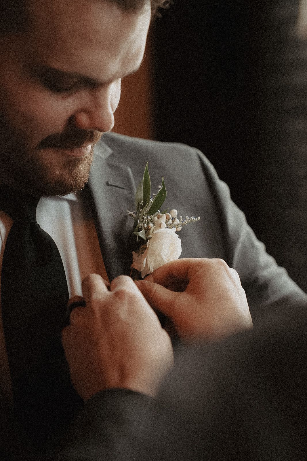 Close-up shot of a boutonniere being pinned on groom with a gray suit jacket at Norther Pacific Events Center Brainerd Minnesota