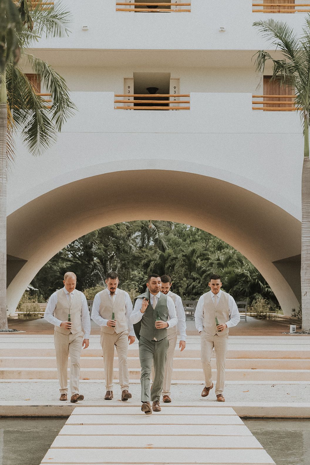 Groomsmen in light colored suits posing under white arches at Secrets Akumal Mexico resort wedding