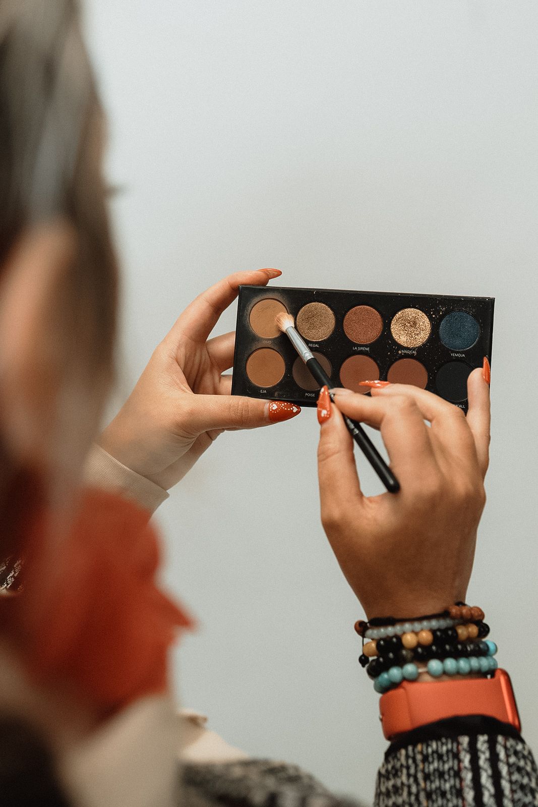 Hands holding and displaying a makeup palette with neutral eyeshadow colors.