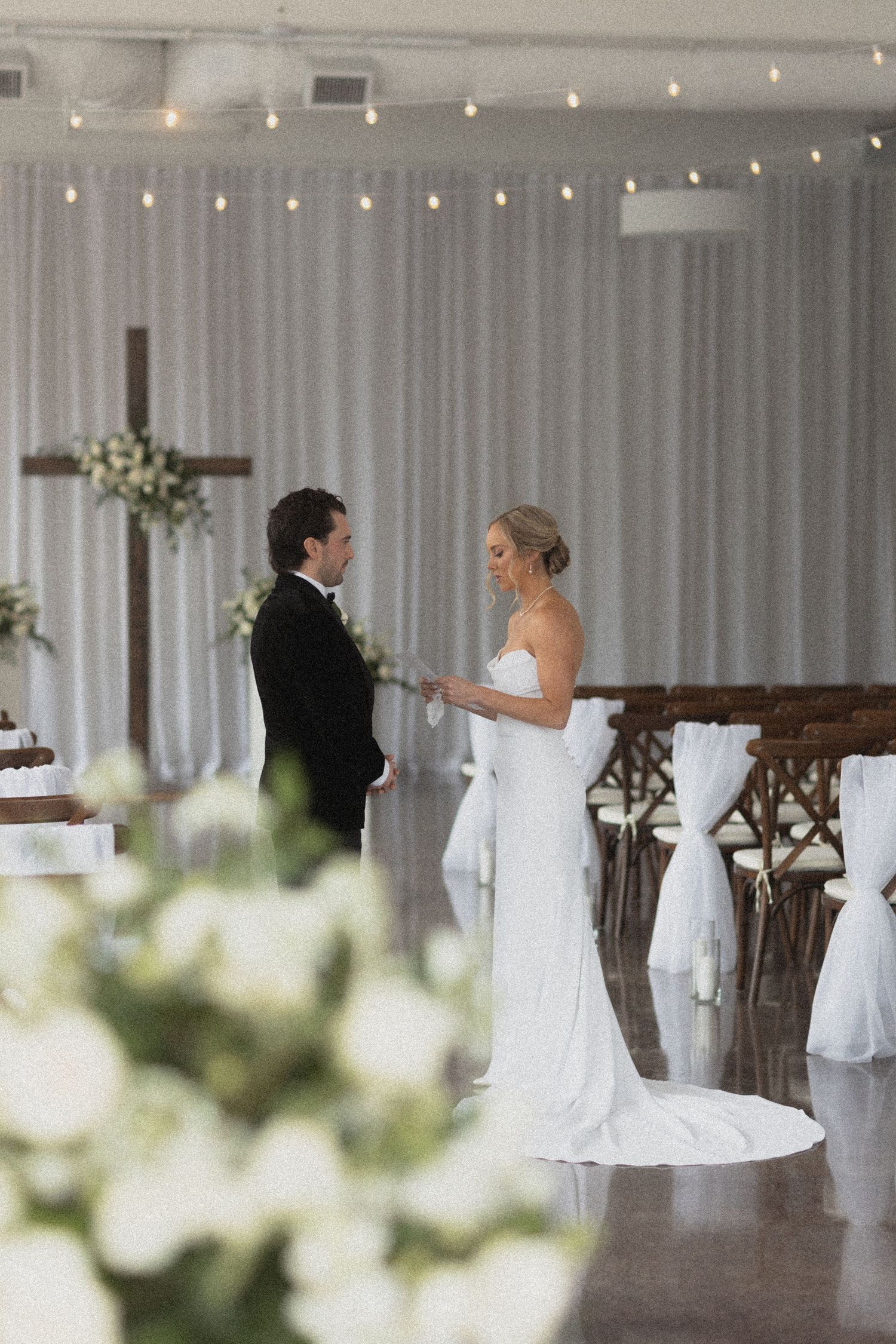 Wedding ceremony setup in elegant white room with string lights and wooden cross altar at Urban Daisy Weddings in Minneapolis Minnesota