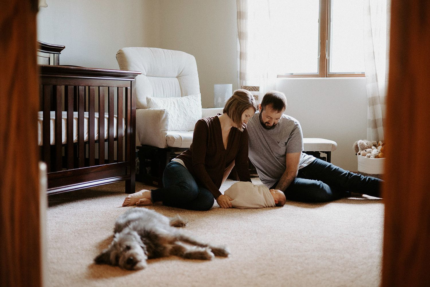 Interior lifestyle scene showing relaxed moments in a sunlit room with wooden furniture. Mom and Dad with new born baby and dog