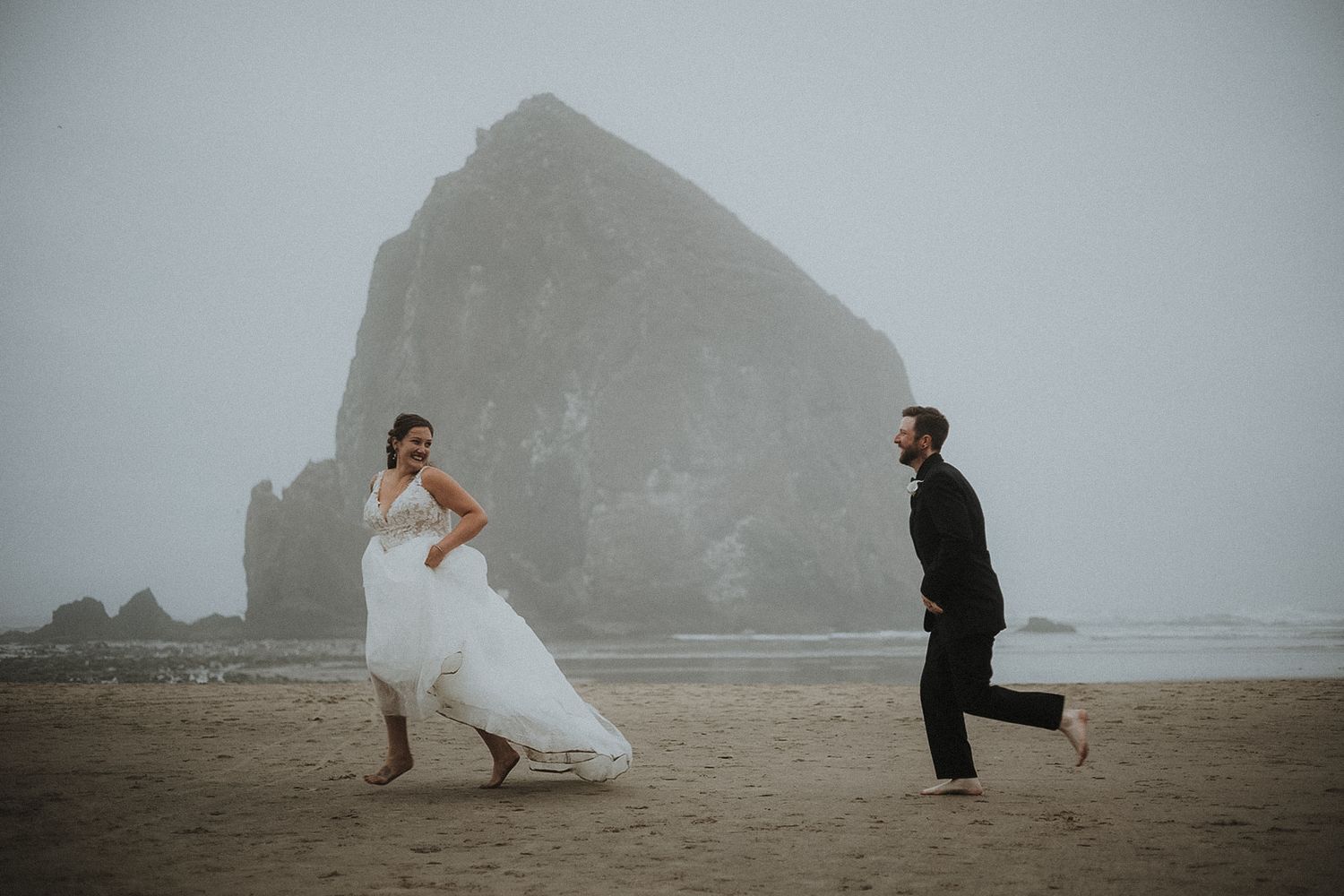 Ethereal beach scene with towering cliffs and Wedding Couple in formal attire on misty shores. Haystack Rock Oregon