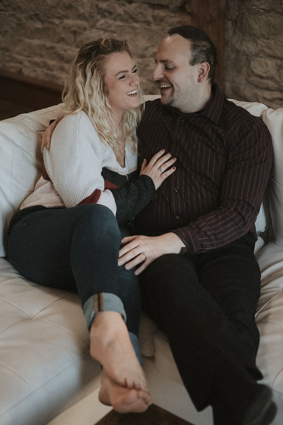 An engaged couple shares an intimate laughing moment together on a cream colored couch in Stillwater Minnesota