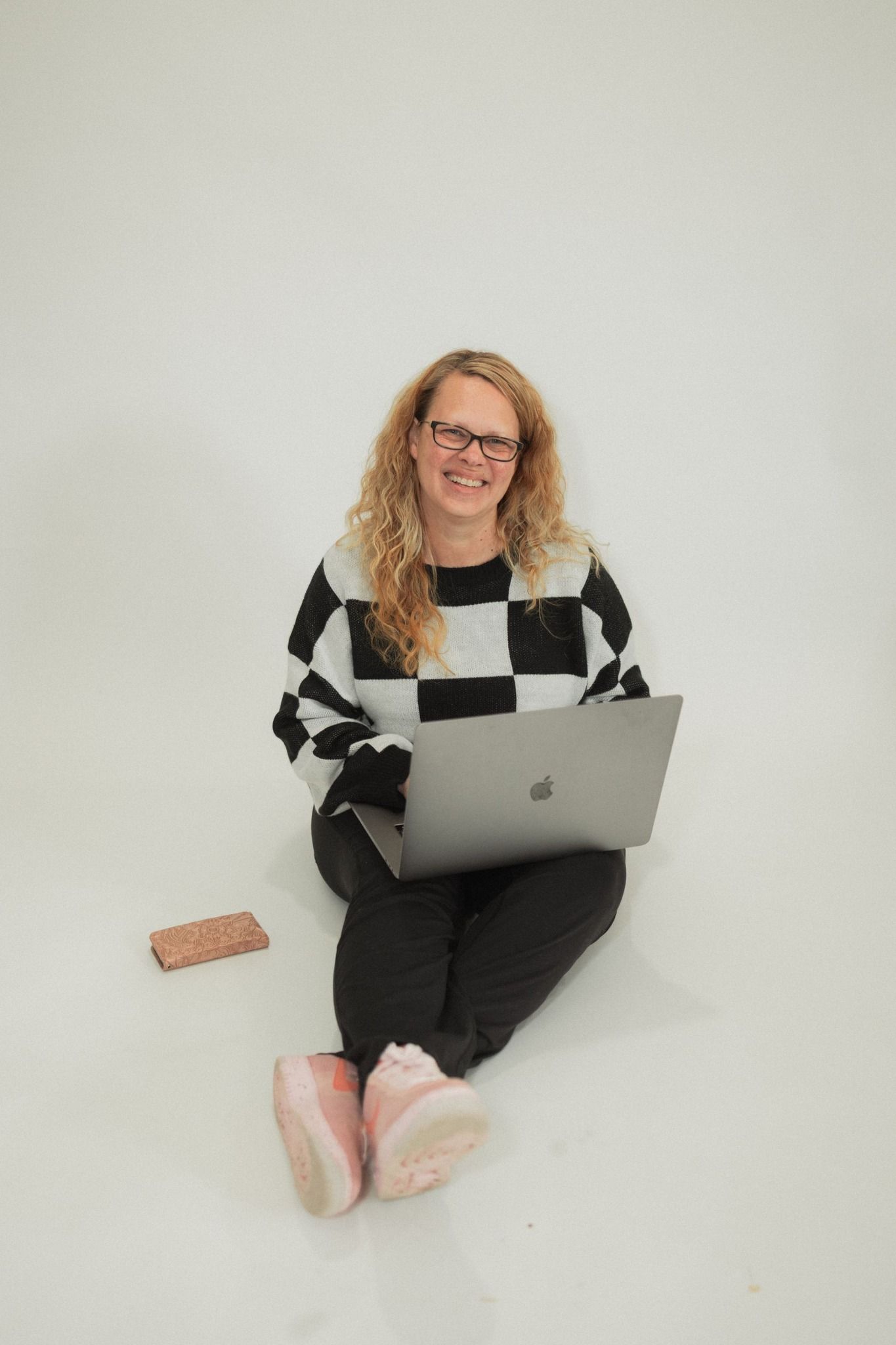 Person in black and white outfit sitting casually with laptop on white background.