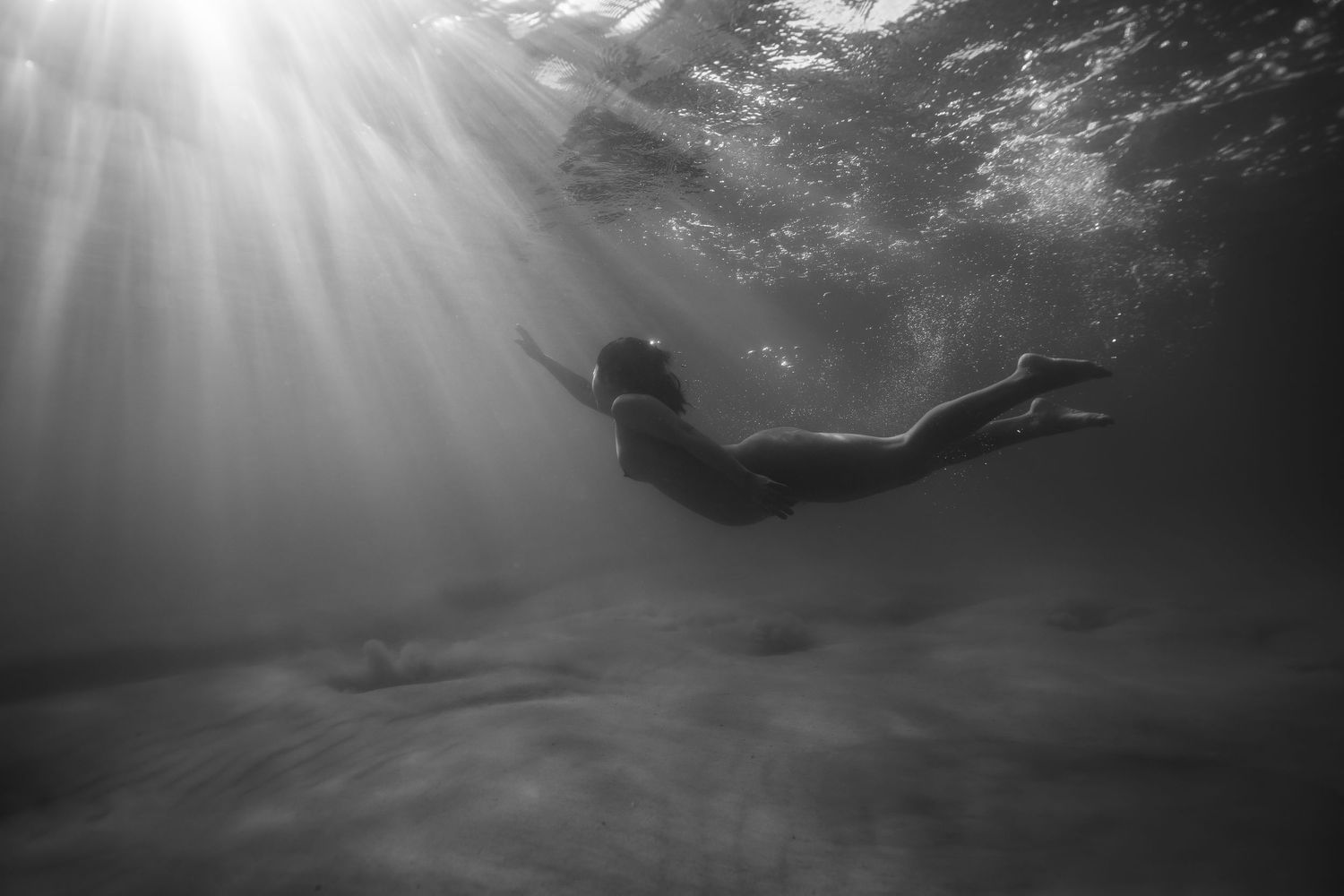 Dramatic black and white underwater shot of diver with sunbeams streaming through water.