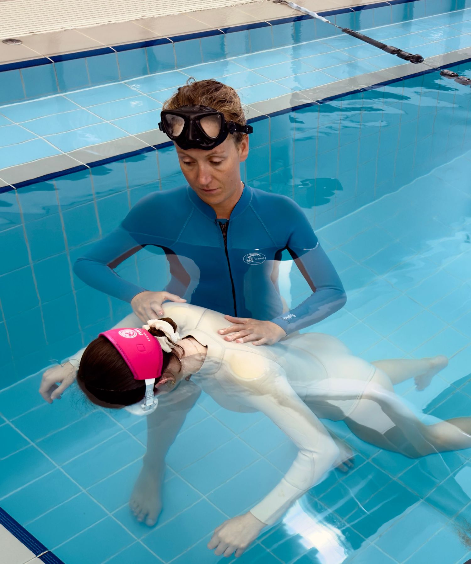 Swimming instructor demonstrates water safety techniques in a pool with clear blue water.