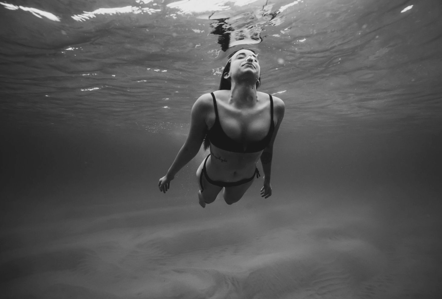 Underwater black and white photography capturing swimming figures beneath the surface.