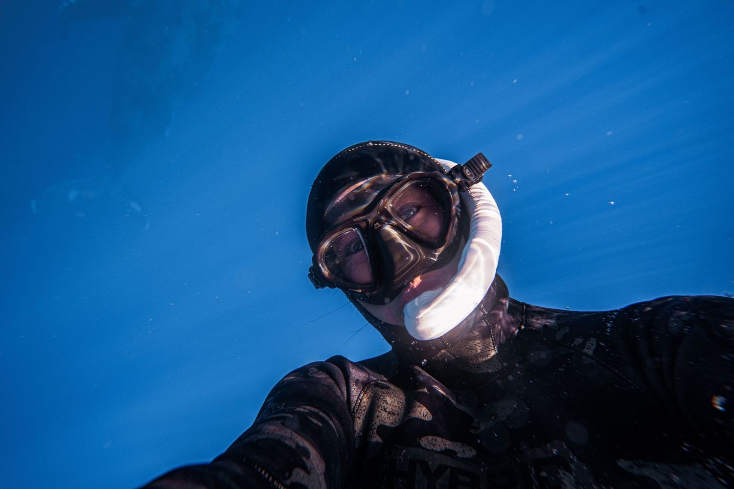Underwater selfie with scuba diving gear against bright blue sky background.