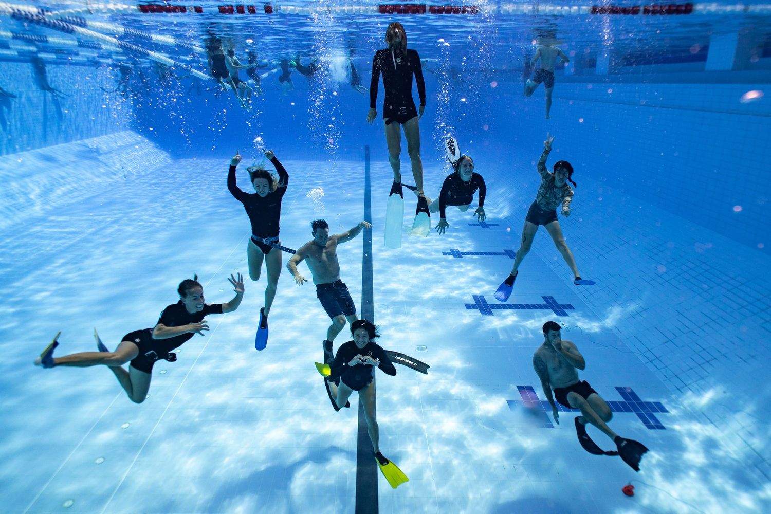 Underwater sequence of people playing volleyball in a swimming pool with a yellow ball.