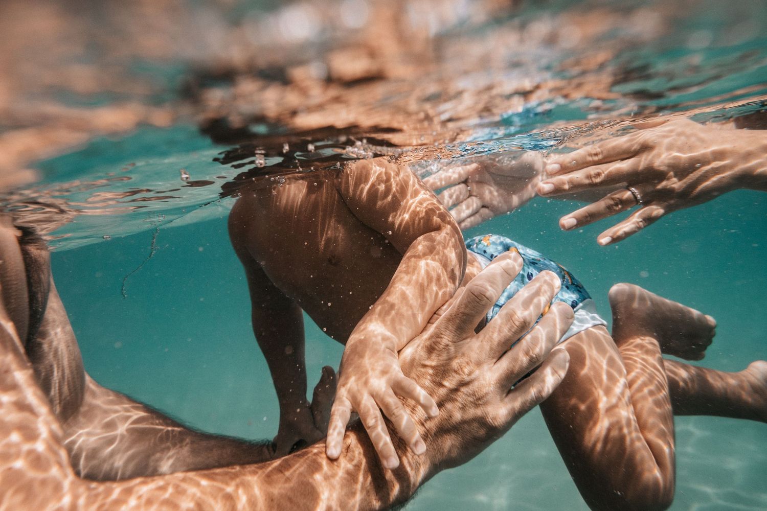 Underwater view of swimmers in crystal clear turquoise water creating rippling patterns.