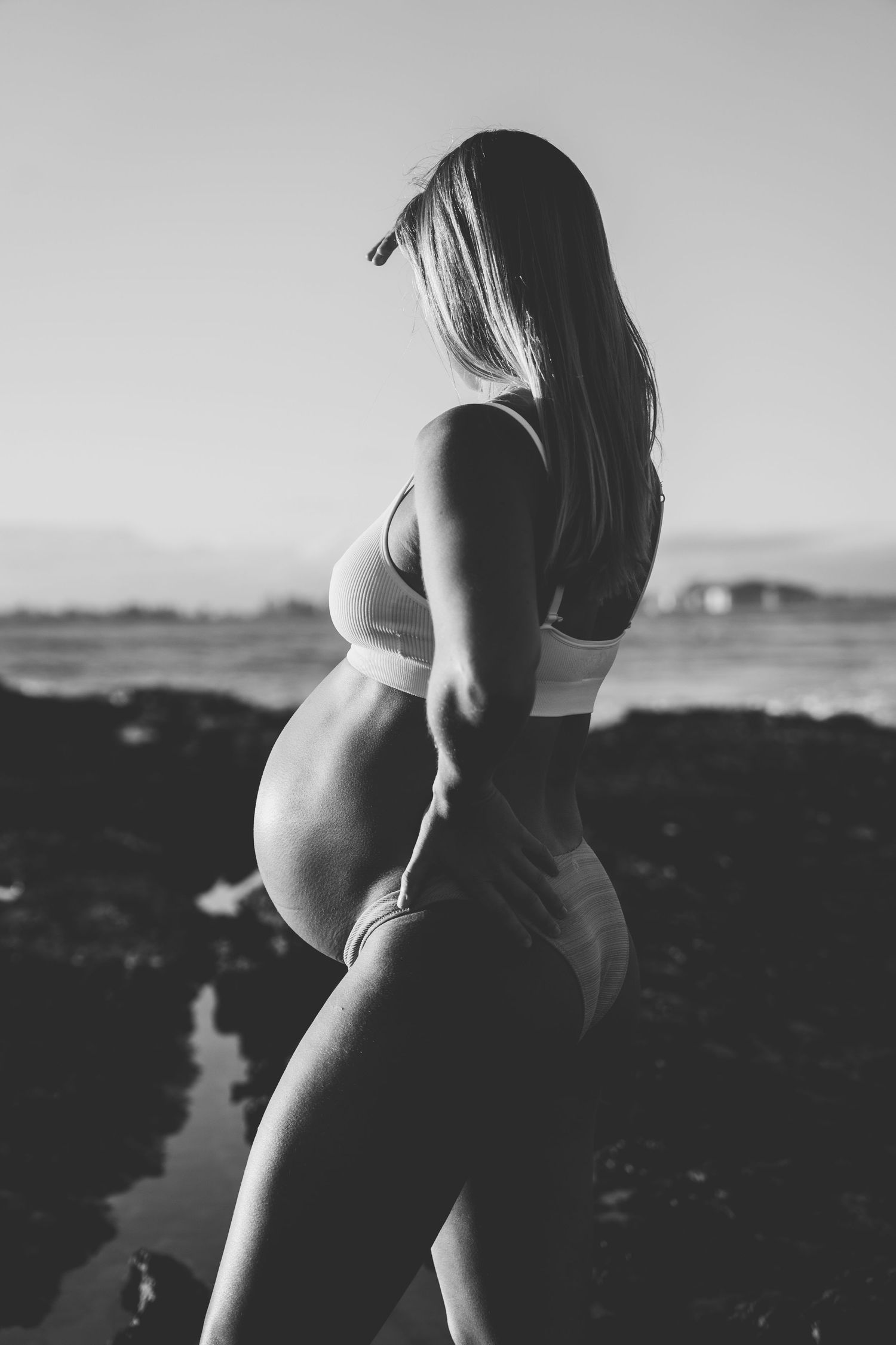 Silhouetted maternity portraits against rocky coastal landscape at sunset.