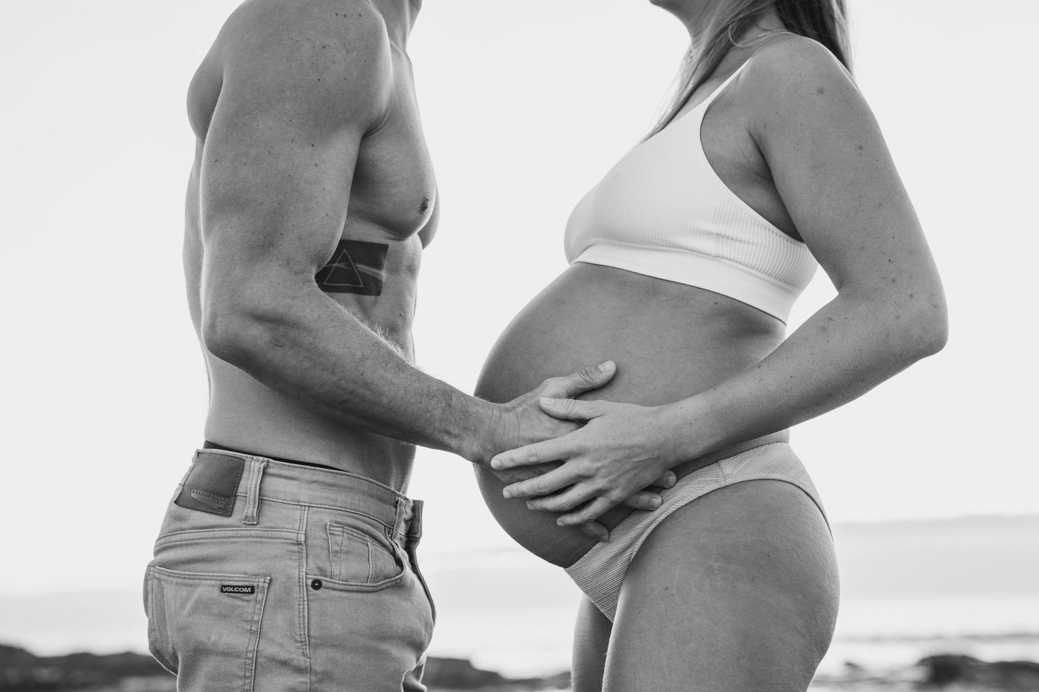 Intimate maternity photography session on beach with couples silhouettes.