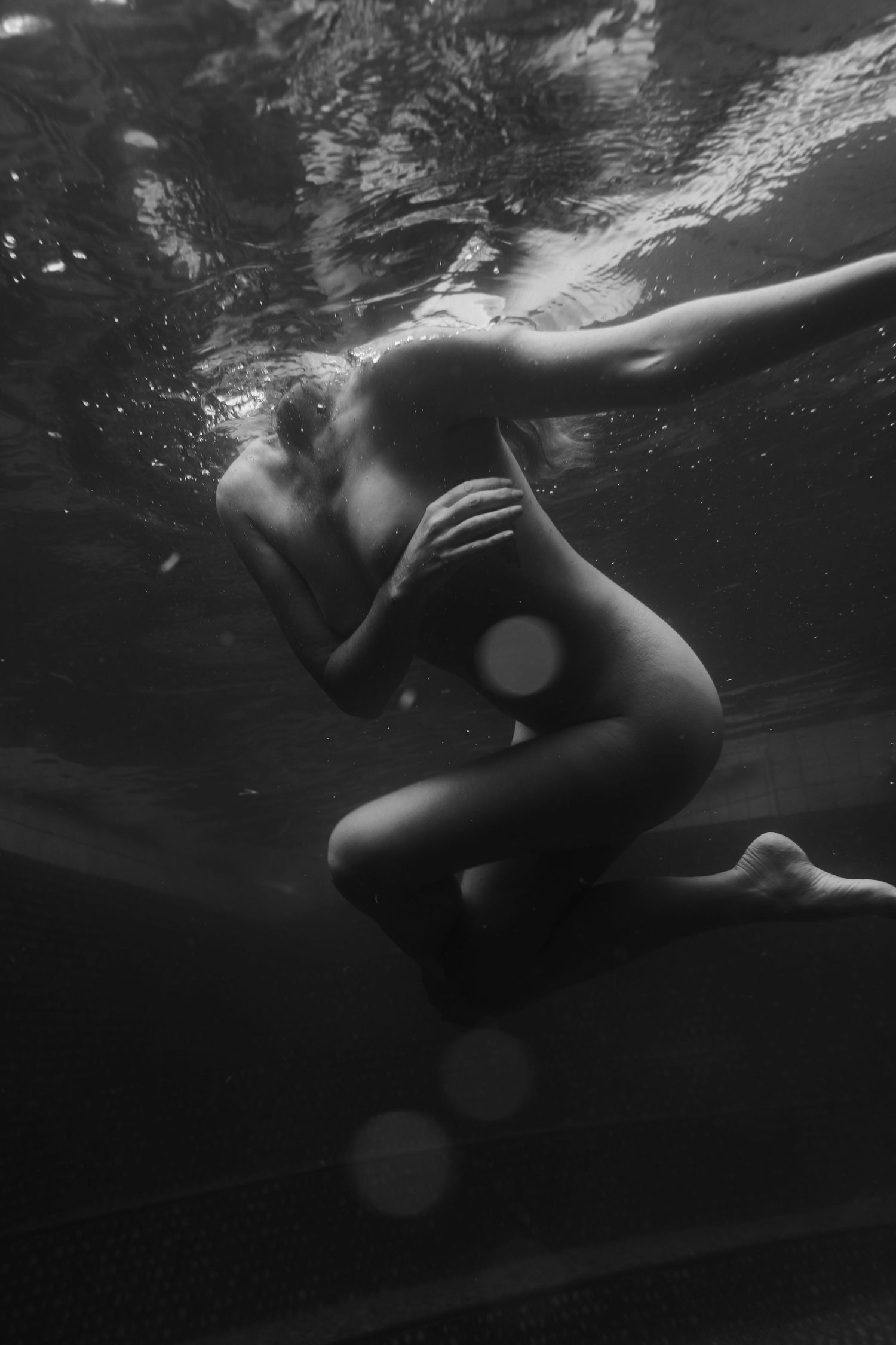 Underwater sequence of a swimmer in a black swimsuit gracefully gliding through dark water.