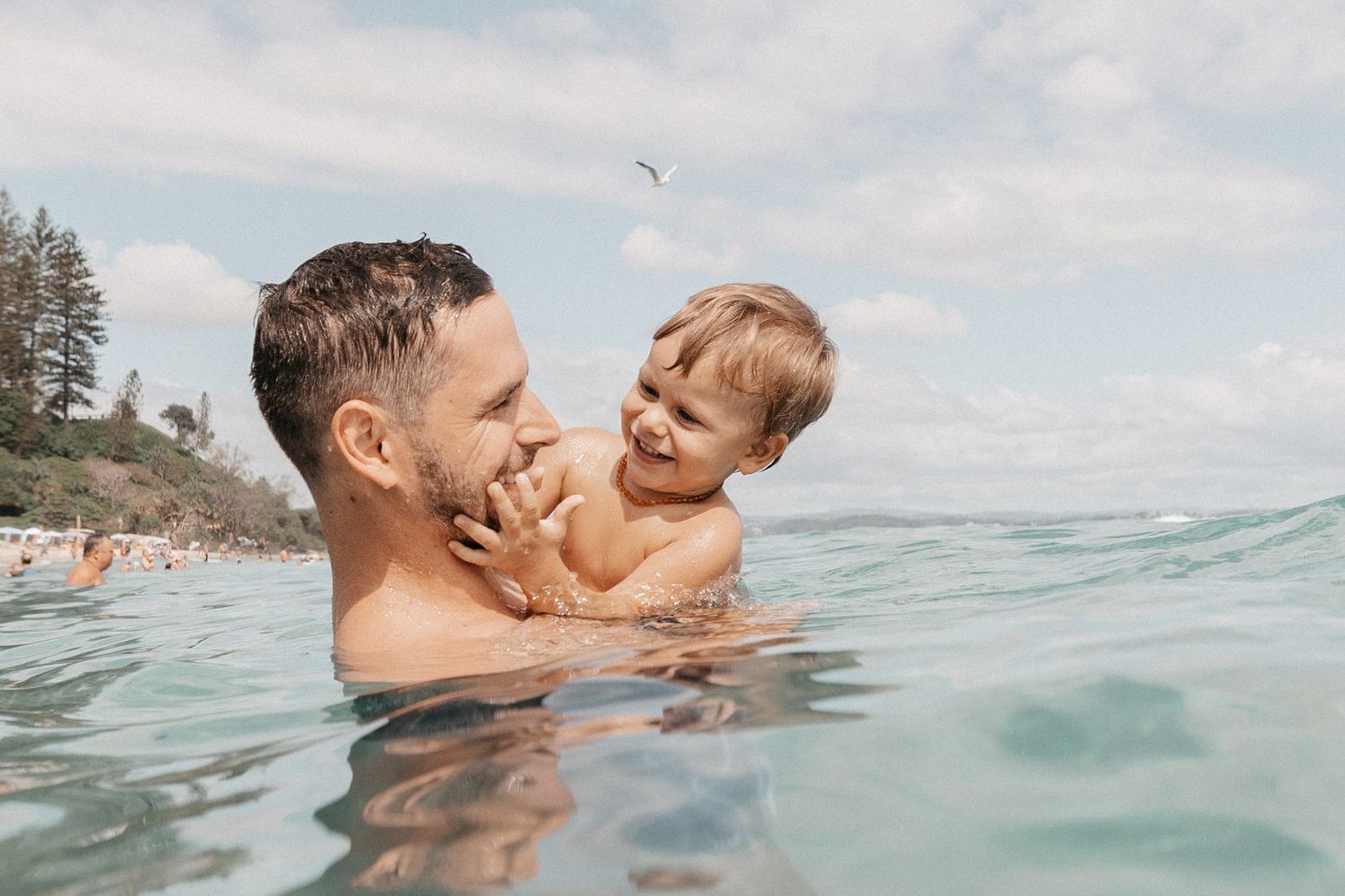 Parent and child playing together in ocean waves on a sunny beach day.