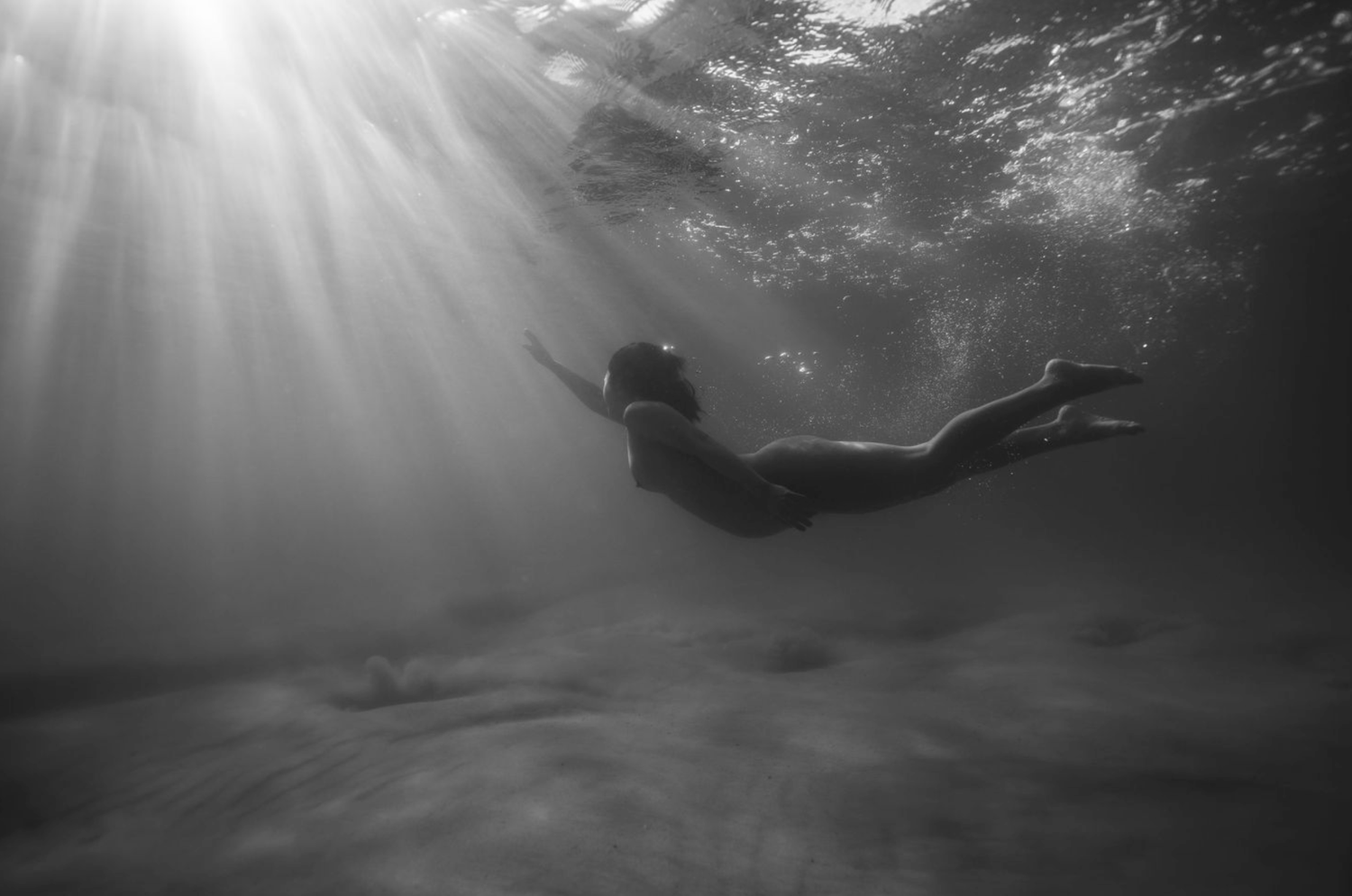 Dramatic underwater sunbeams piercing through dark waters creating mystical lighting effects.