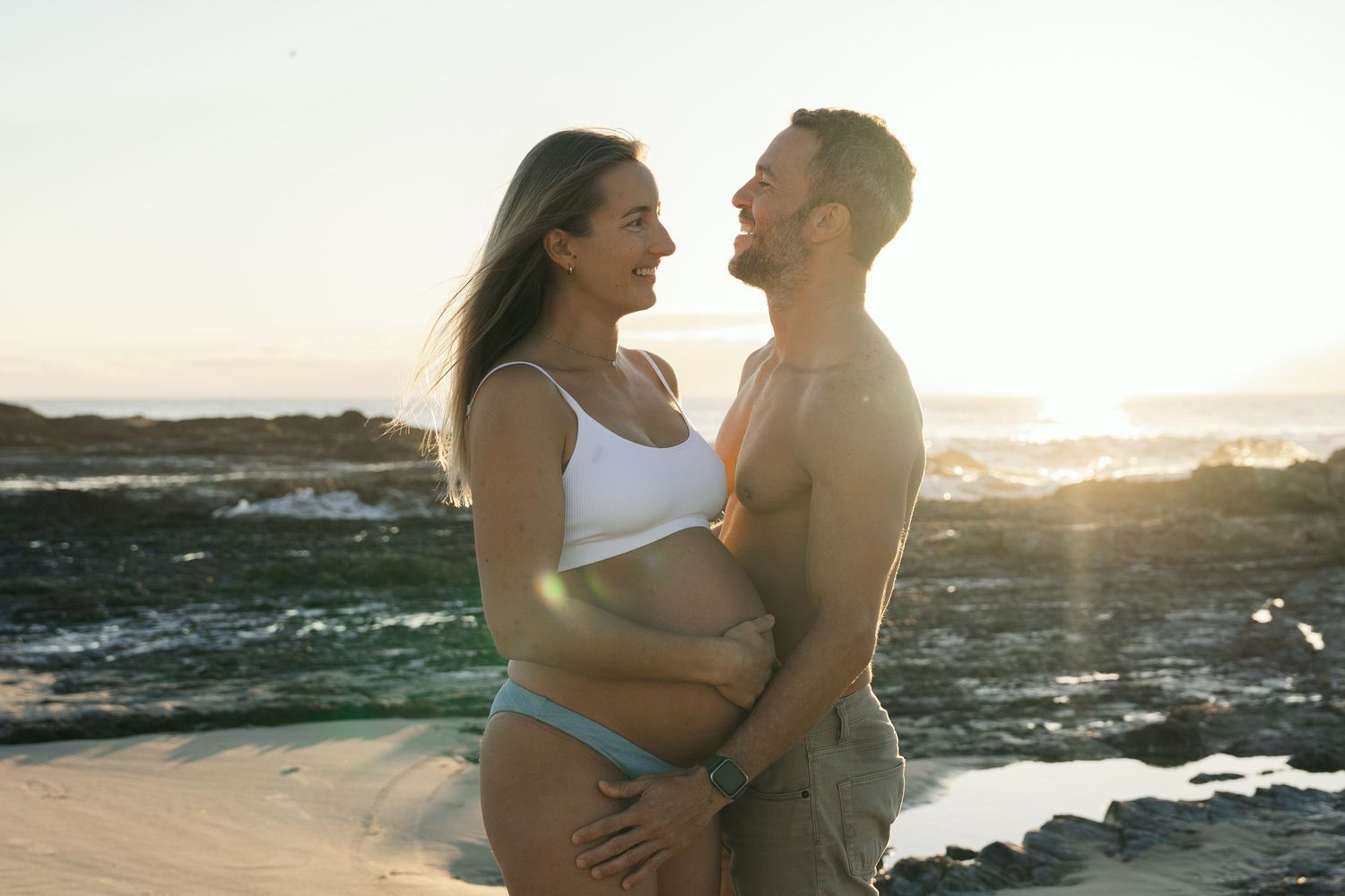 Romantic beach photoshoot with couple embracing against ocean backdrop at golden hour.