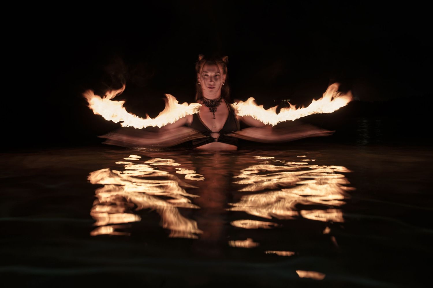 Dramatic fire performance reflected in dark water creating glowing patterns.