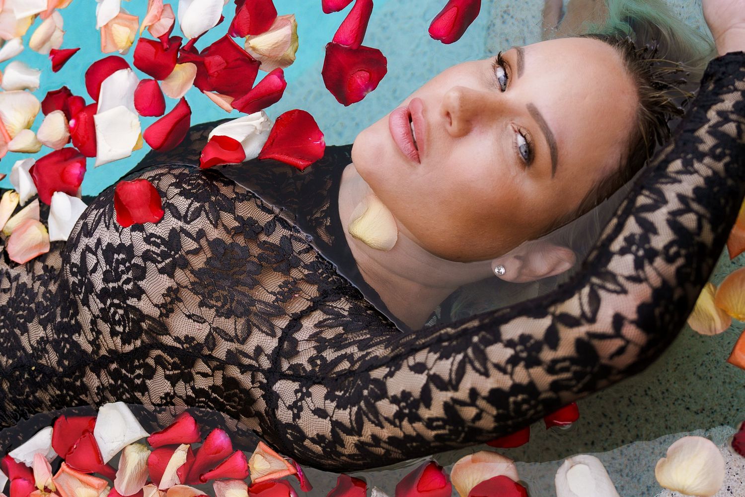 A person lying on a floral surface surrounded by scattered red heart-shaped petals in a romantic setting.
