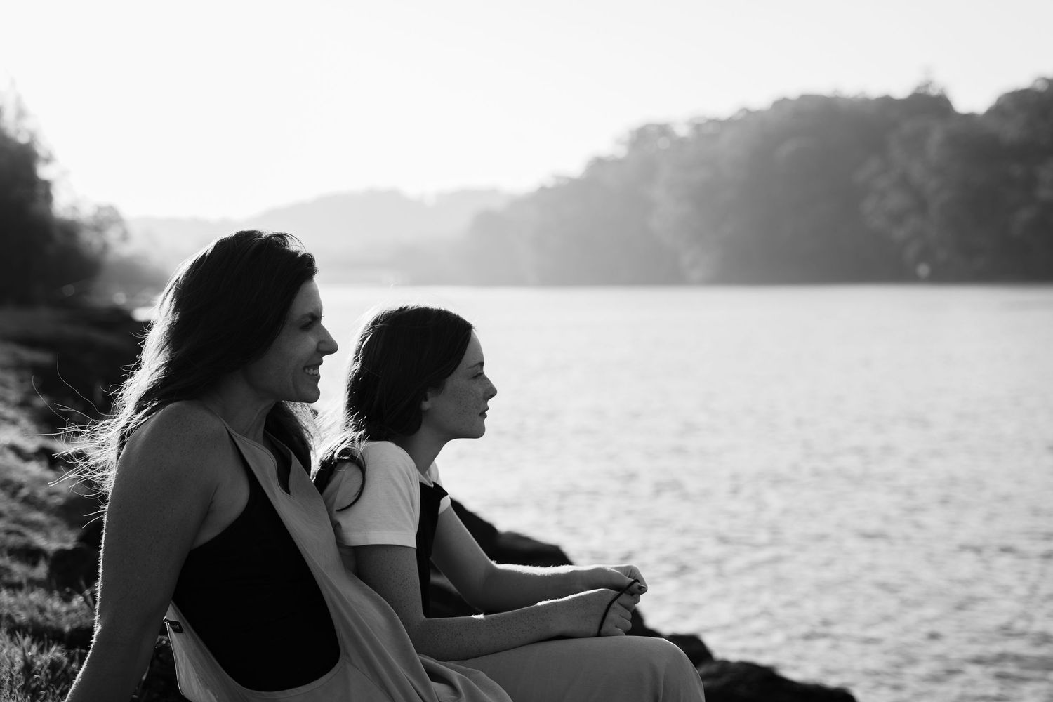 Two silhouettes sitting by a misty lake at sunset.