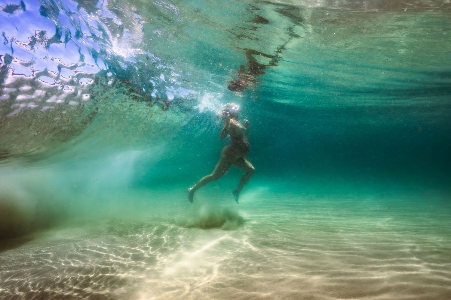 Crystal clear turquoise waters with sandy ocean floor and rippling sunlight patterns.