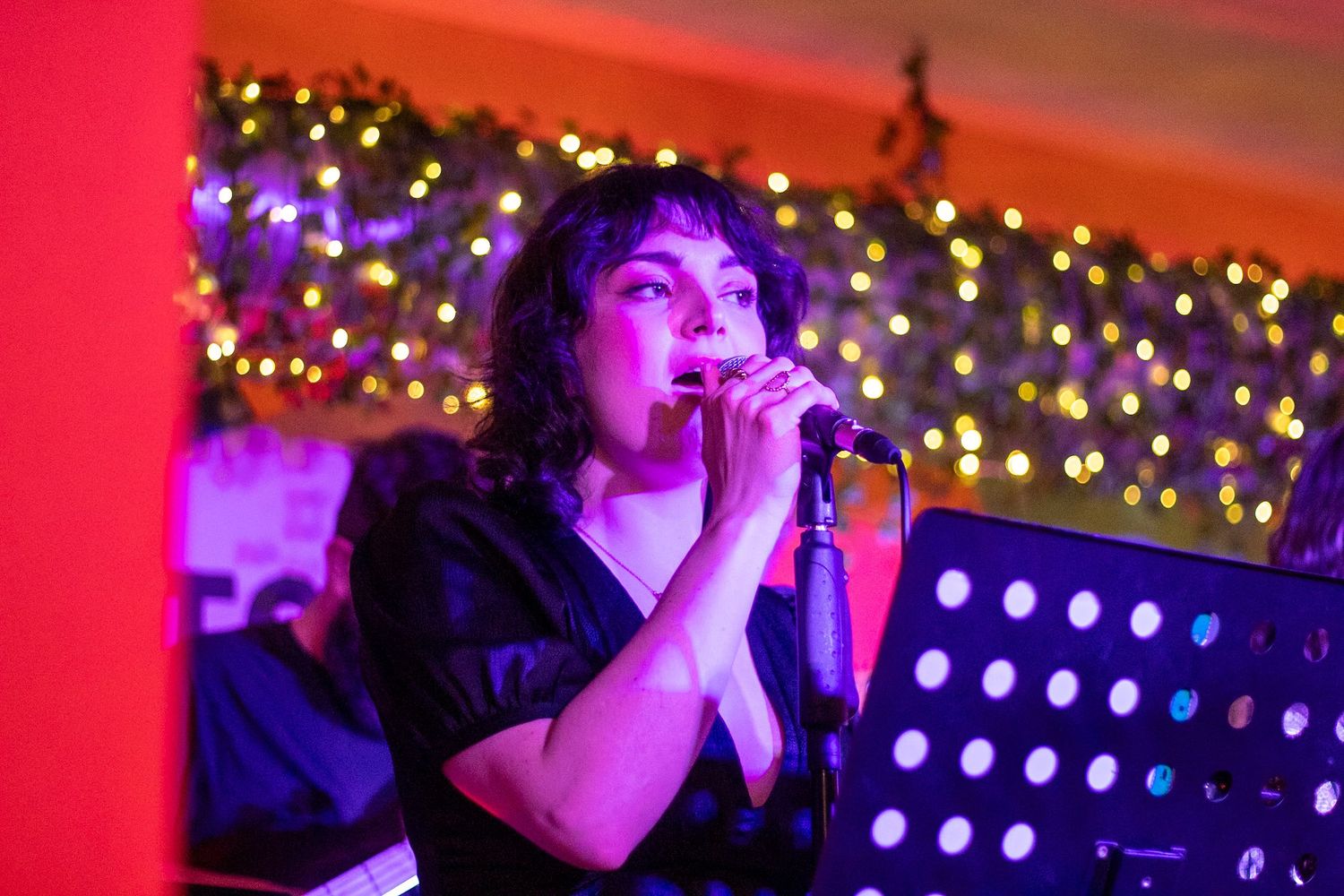 Female singer performing on stage holding microphone with colorful Christmas lights in the background.