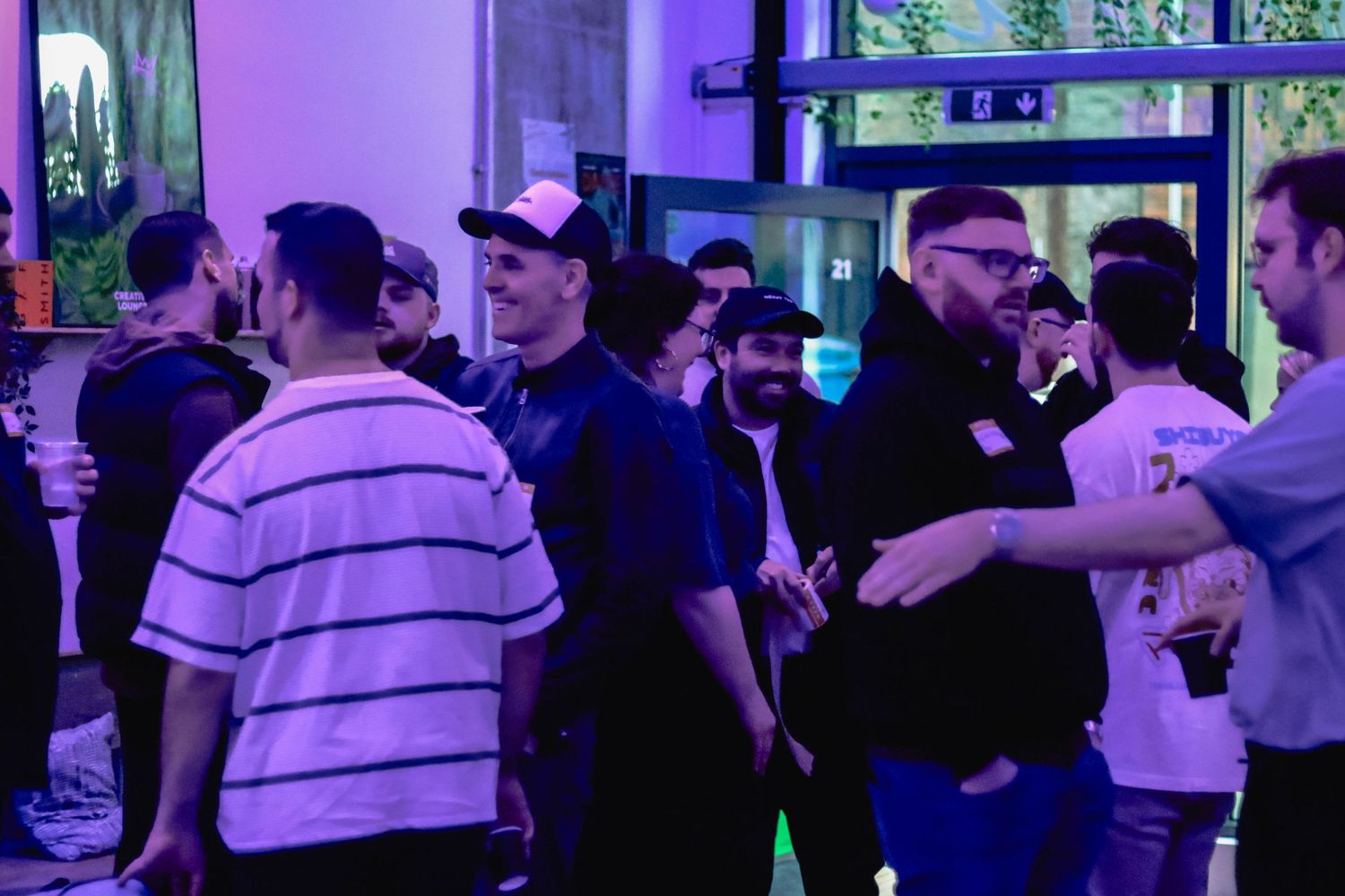 Group of people socializing at an indoor networking event with purple ambient lighting.