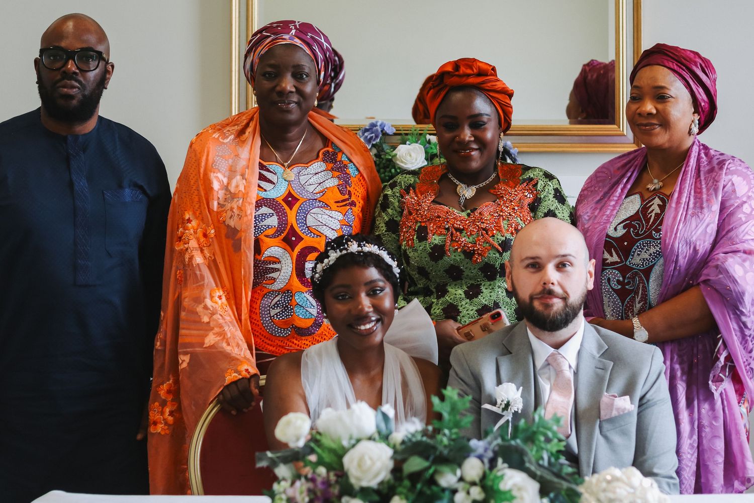 Wedding couple seated at table with four family members in vibrant African attire posing for a formal group photo.
