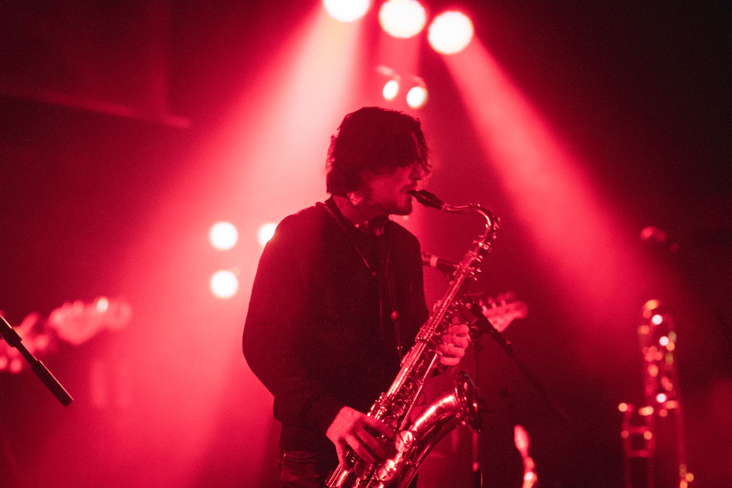 Musician playing saxophone on stage under dramatic red stage lighting during a live concert performance.