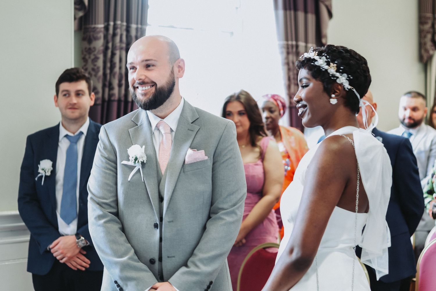 A smiling bald groom in grey suit meets his radiant Black bride during a wedding ceremony.