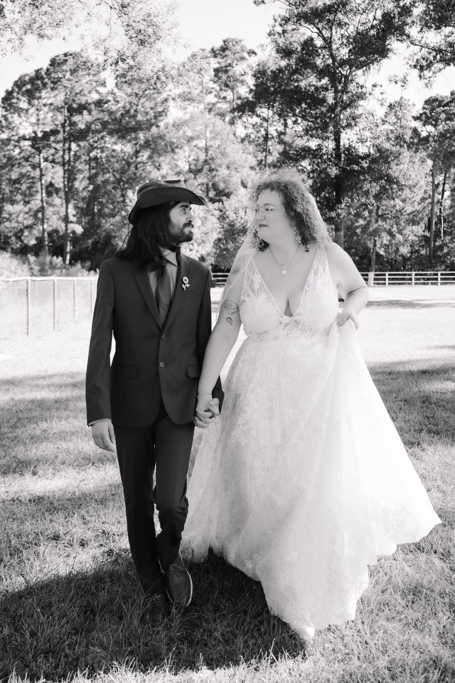 Black and white photo of a bride and groom holding hands and walking outdoors on their wedding day.