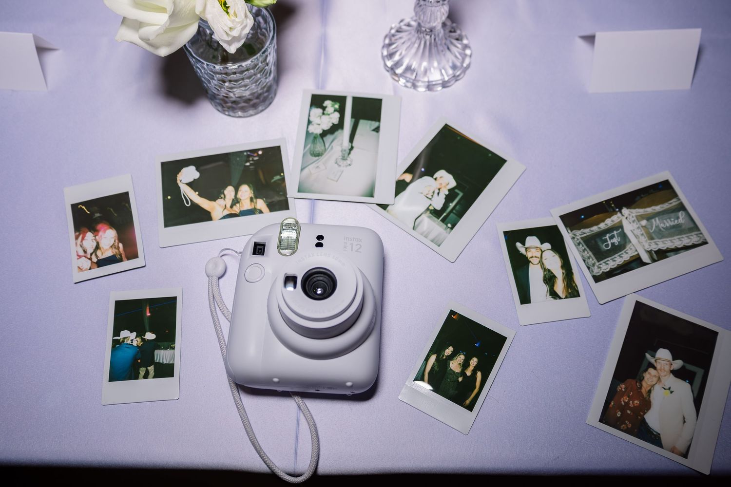 Fujifilm Instax mini camera surrounded by polaroid photos on a white table at a wedding reception.