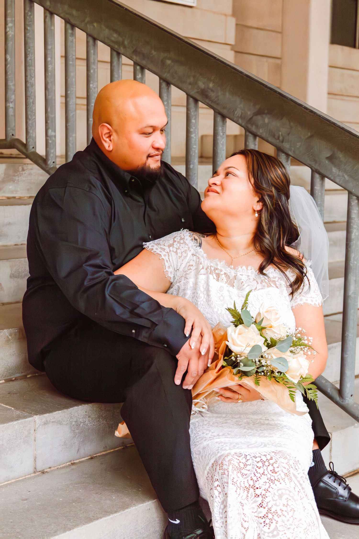 Newlywed couple sitting on stone steps sharing a tender moment with bridal bouquet.