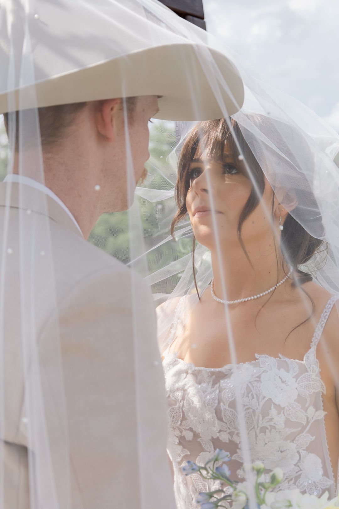 Bride and groom share an intimate moment under a sheer wedding veil outdoors on their wedding day.