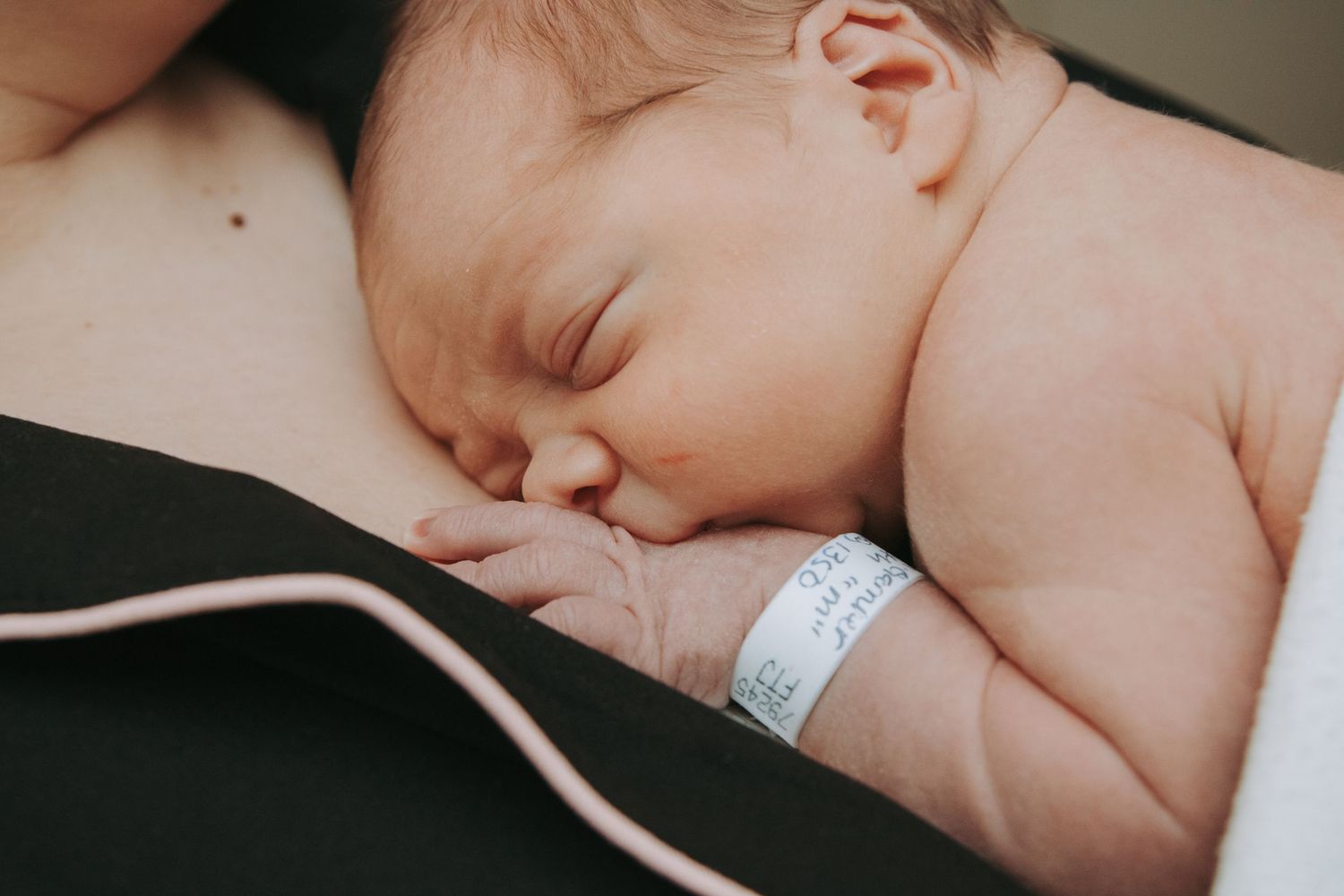 Peaceful newborn baby sleeping on mother's chest wearing hospital identification bracelet.