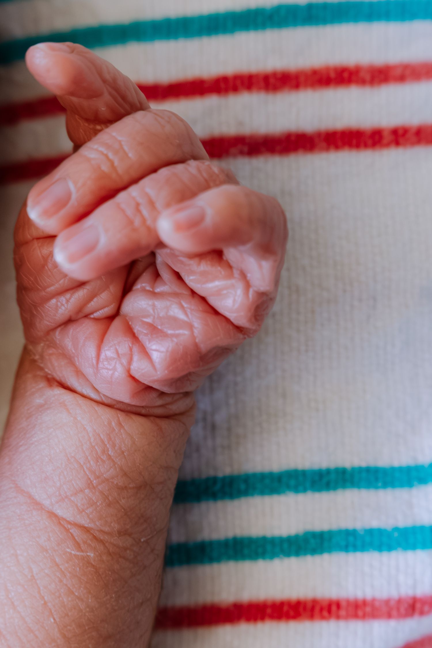 Close-up of a newborn baby's tiny clenched fist resting on a striped blanket.
