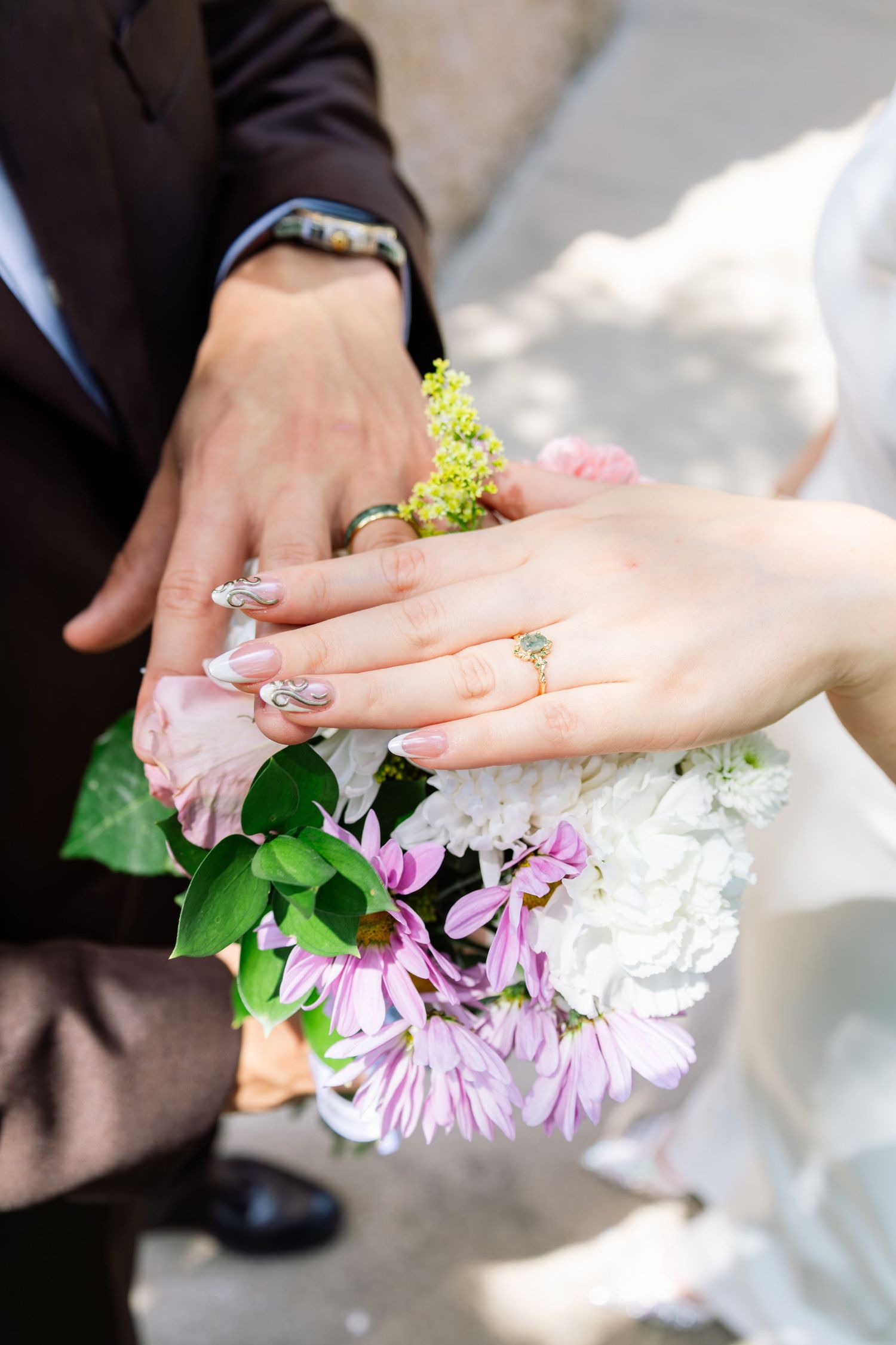 Newlyweds display wedding rings on hands resting over a bouquet of pink and white flowers.