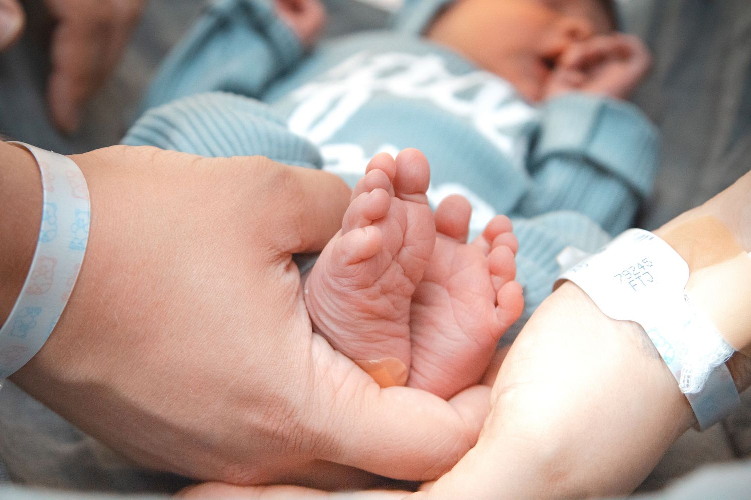 Adult hands gently cradle tiny newborn baby feet in a tender hospital moment.