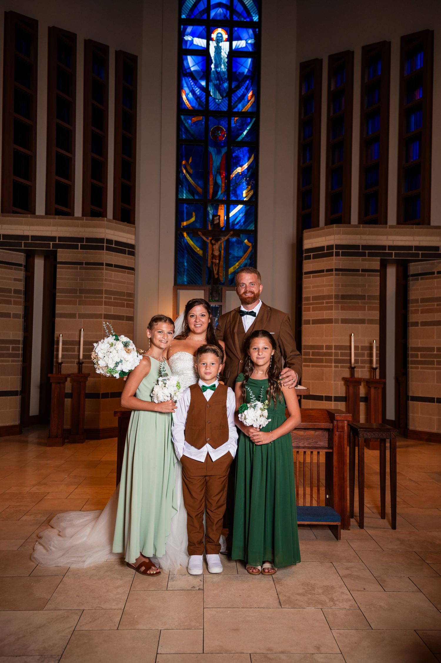 Wedding family portrait with bride, groom, and three children in green attire inside a church.