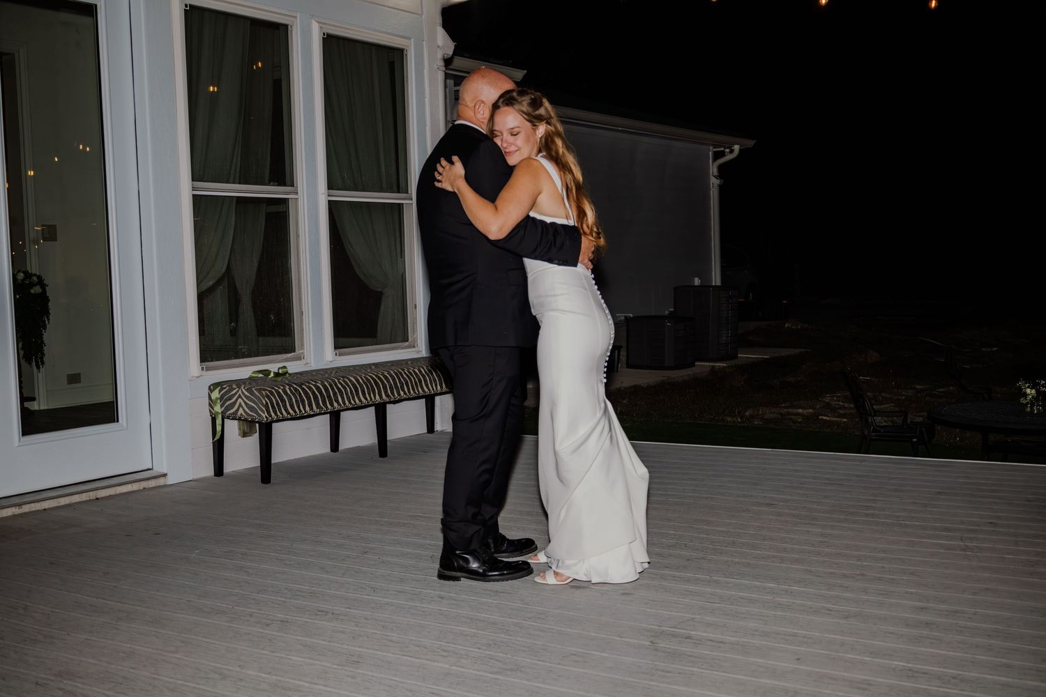 Bride and groom sharing a romantic slow dance together on an outdoor patio at night.