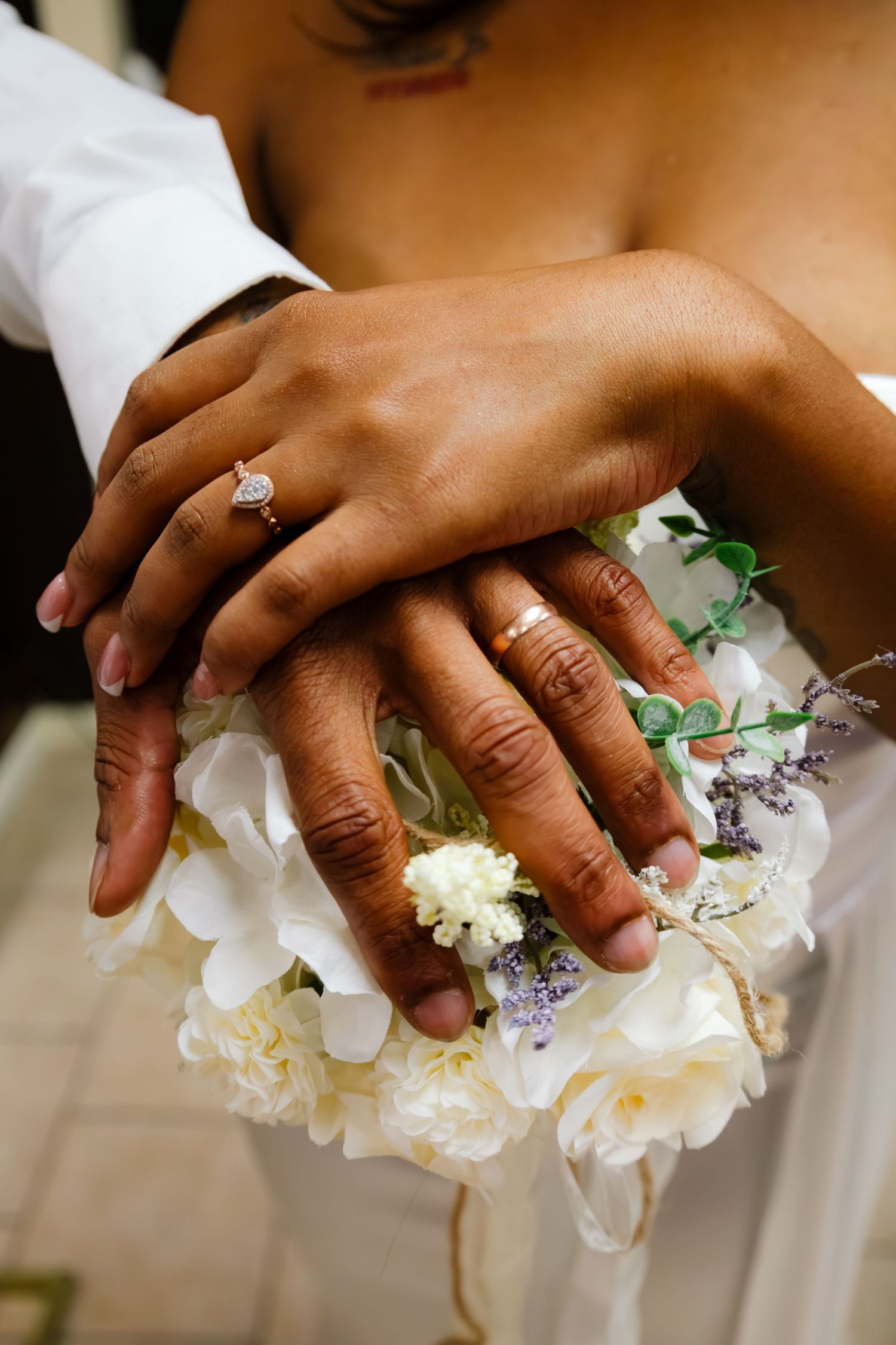 Close-up of newlywed couple's hands displaying wedding rings resting on a white floral bouquet.