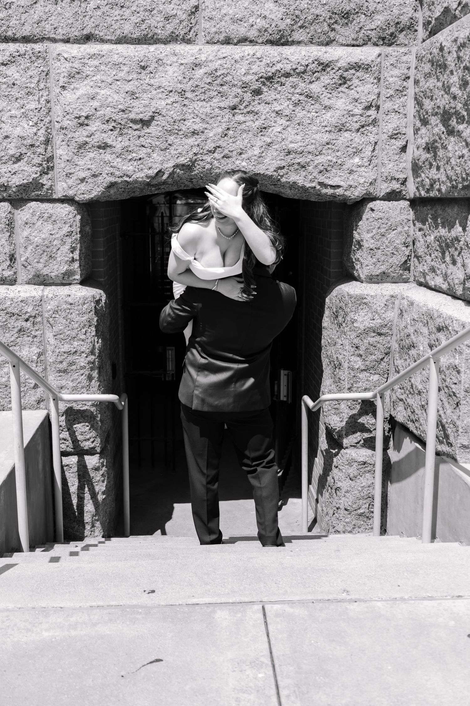 Black and white photo of a couple embracing at the entrance of a stone building on their wedding day.